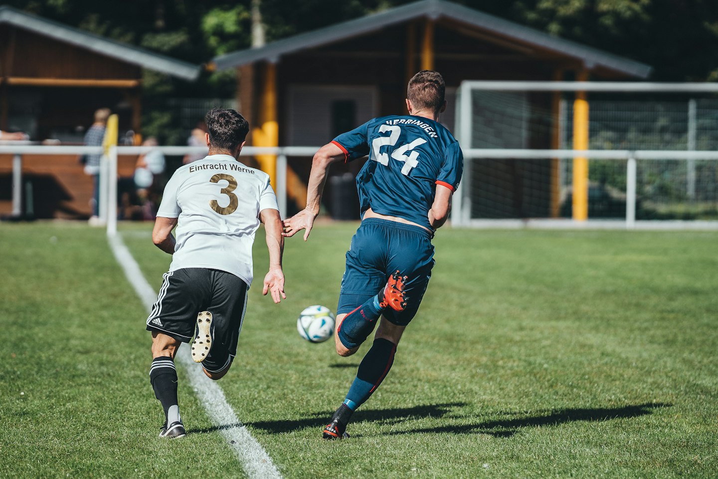 Two soccer players run on a green field with one dribbling the ball.